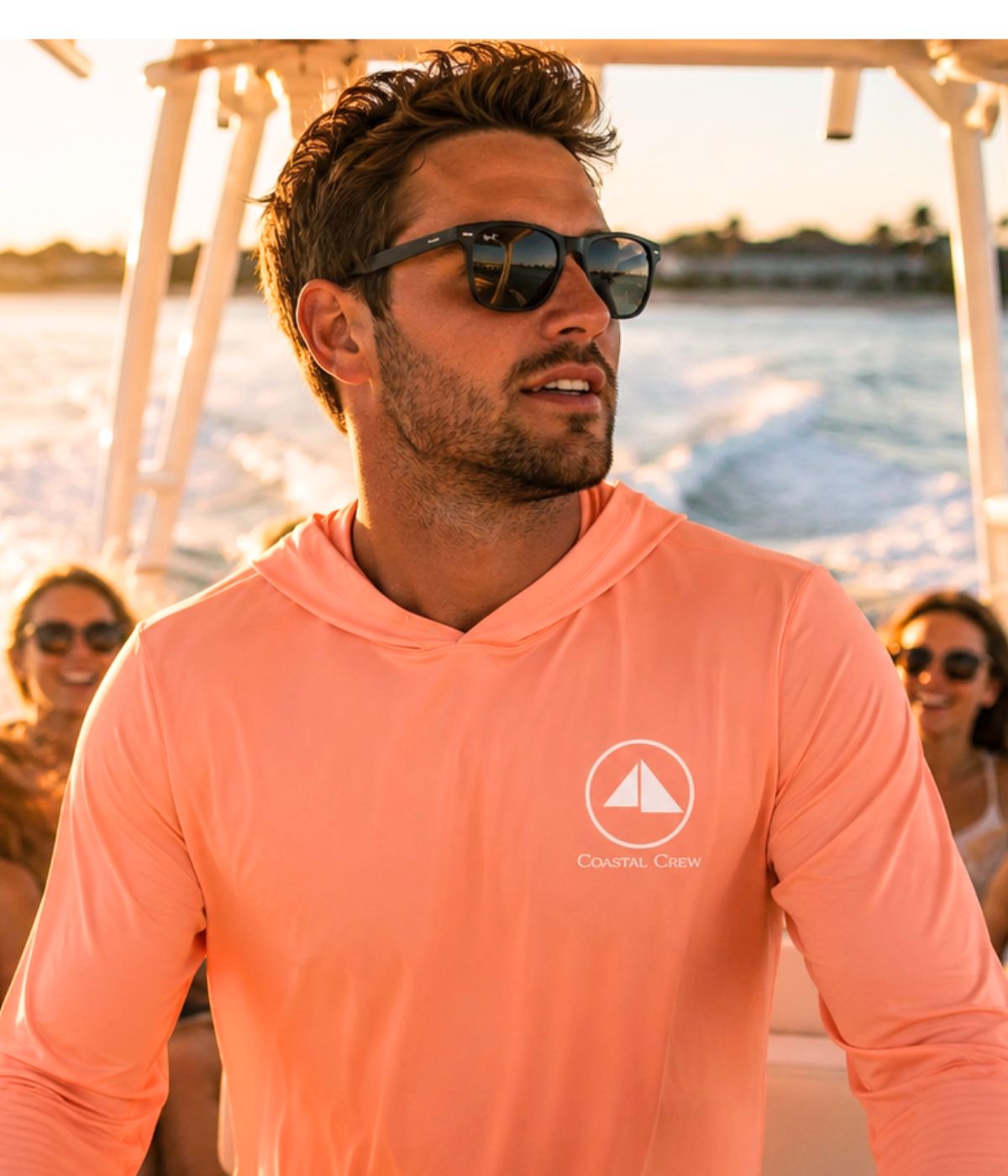 Man wearing a coral Sunrise UV Hoodie on a boat at sunset